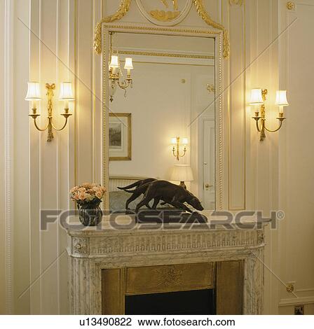 Lighted wall-lights on either side of overmantel mirror above mantelpiece with animal statue View Large Photo Image Stock Image - Lighted wall-lights on either side of overmantel mirror above mantelpiece with animal statue. Fotosearch
