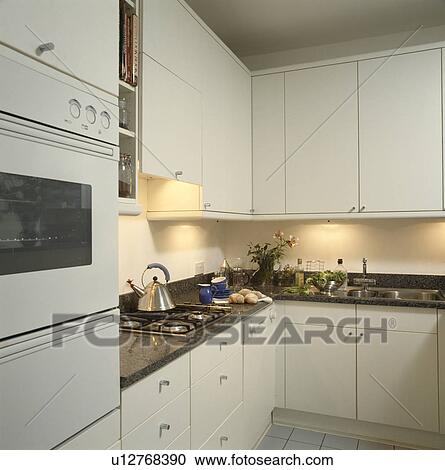 Lighting below fitted cupboards in modern white kitchen with granite worktops View Large Photo Image Stock Image - Lighting below fitted cupboards in modern white kitchen with granite worktops. Fotosearch