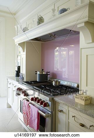 Stock Photo - Lilac glass splashback above range oven in cream Mark Wilkinson kitchen with grey marble worktops. Fotosearch