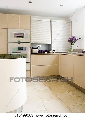 Stock Image - Limestone flooring in modern white kitchen with fitted cream units. Fotosearch