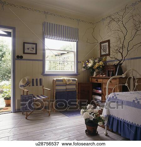 Stock Photo - Limewashed wooden floor in simple bedroom with blue striped blind on window. Fotosearch