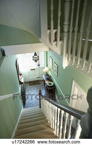 Stock Photograph - Looking down staircase with white bannisters and cream carpet to green hall with tessellated tiled floor. Fotosearch