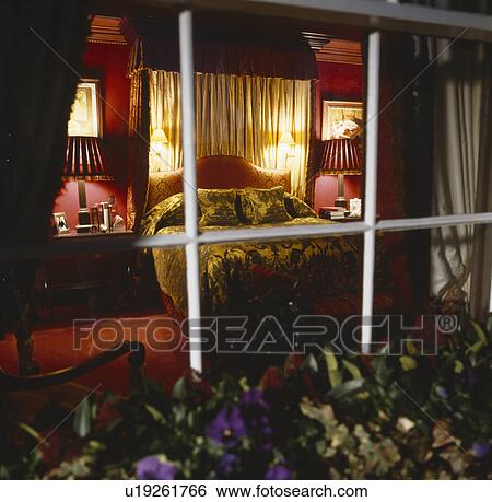 Stock Photograph - Looking through window into red bedroom with wall-lights on half-tester bed with cream drapes and velvet bedcover. Fotosearch