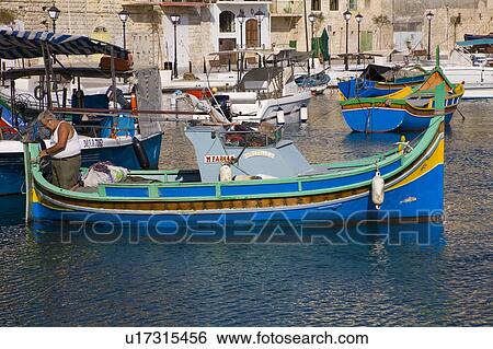 Stock Photograph - Luzzu fishing boat moored in Saint Julian’s Harbour, Spinola Bay, Saint Julian’s, Malta. Fotosearch