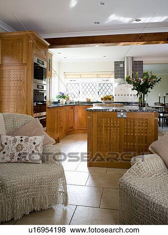 Stock Photo - Macrame throws on comfortable armchairs in cottage kitchen with travertine flooring and fitted wooden units. Fotosearch