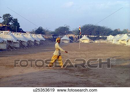 Stock Photo - Man in traditional Rajastani dress walking across compound with tents. Fotosearch