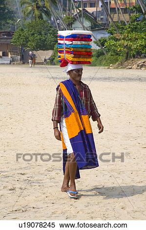 Stock Photography - Man walking on Kovalam Beach carrying tablecloths on his head, Kovalam, Kerala, India. Fotosearch