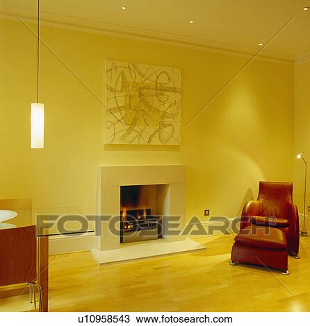 Stock Image - Matthew Hilton "Balzac" armchair and ottoman in modern yellow living room with abstract painting above fireplace. Fotosearch