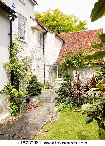 Stock Image - Metal arch above path beside white country house. Fotosearch