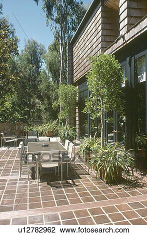 Stock Image - Metal chairs and table on quarry-tiled patio in front of sixties house. Fotosearch