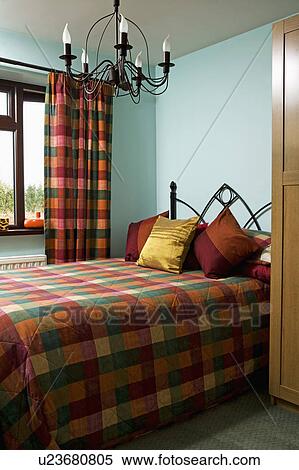 Stock Photography - Metal chandelier in pastel turquoise bedroom with multicoloured checked quilt and matching curtains. Fotosearch