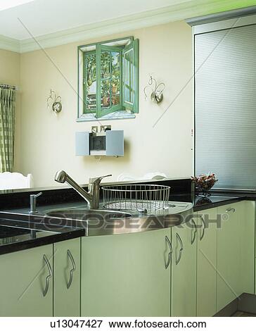 Stock Photo - Metal drainer and stainless steel sink in curved fitted unit in modern kitchen with small trompe-l'oeil window on wall. Fotosearch