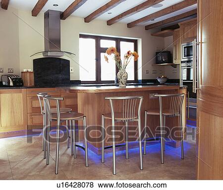 Metal stools at breakfast bar in modern country kitchen with blue halogen lighting below fitted cupbaords View Large Photo Image Stock Photo - Metal stools at breakfast bar in modern country kitchen with blue halogen lighting below fitted cupbaords. Fotosearch