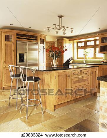 Picture - Metal stools at breakfast bar on oak island unit in country kitchen with limestone flooring. Fotosearch