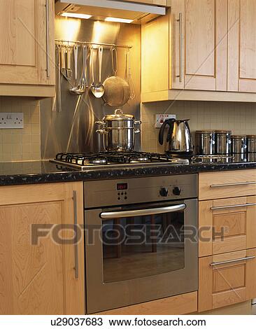 Stock Image - Metal utensils on rack above stainless steel oven in modern kitchen. Fotosearch