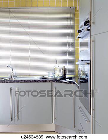 Metallic slatted blind above sink in modern kitchen with pale grey units View Large Photo Image Stock Photo - Metallic slatted blind above sink in modern kitchen with pale grey units. Fotosearch