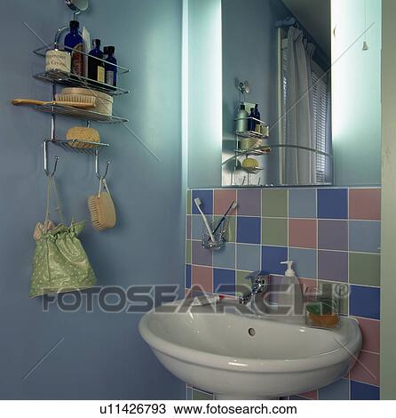 Stock Image - Mirror and pastel tiles above basin in pale turquoise economy-style bathroom. Fotosearch