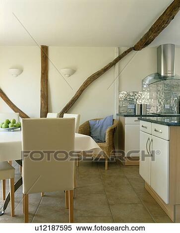 Stock Photography - Modern cream upholstered high-back chairs in cream cottage kitchen with limestone flooring. Fotosearch