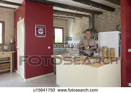 Stock Image - Modern kitchen in stone building with neutral coloured materials and beamed ceiling with red feature wall.. Fotosearch