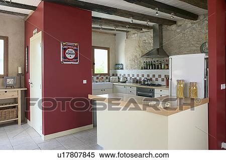 Stock Photography - Modern kitchen in stone building with neutral coloured materials and beamed ceiling. Modern kitchen in stone building with neutral coloured materials and beamed ceiling with red feature wall.. Fotosearch
