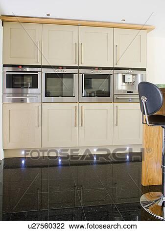 Modern kitchen with eye-level double ovens in row in fitted cream units with recessed lighting on kick-boards View Large Photo Image Stock Image - Modern kitchen with eye-level double ovens in row in fitted cream units with recessed lighting on kick-boards. Fotosearch