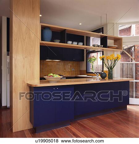 Stock Photo - Modern kitchen with wooden shelving above blue fitted unit. Fotosearch