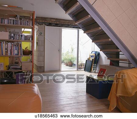 Stock Image - Modern open-plan living room with wooden flooring and orange leather stool and patio doors to the garden. Fotosearch