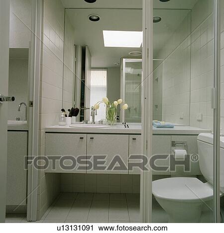 Modern white bathroom with large mirror above fitted vanity unit View Large Photo Image Stock Image - Modern white bathroom with large mirror above fitted vanity unit. Fotosearch