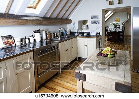 Stock Photo - Old butchers block in modern kitchen with low apex ceiling and stainless steel oven in fitted cream units. Fotosearch