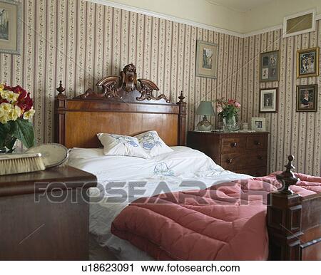 Old Fashioned Pink Eiderdown On Antique Mahogany Bed In Country Bedroom With Patterned Wallpaper Stock Image
