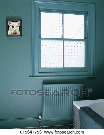 Stock Image - Opaque glass window above painted radiator in blue-green townhouse bathroom. Fotosearch