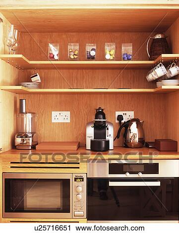 Stock Image - Open shelving above chrome toaster and kettle on worktop with food processor. Fotosearch