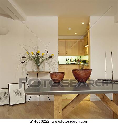 Stock Image - Orange glass bowls on stainless steel and wood table in modern white dining room. Fotosearch