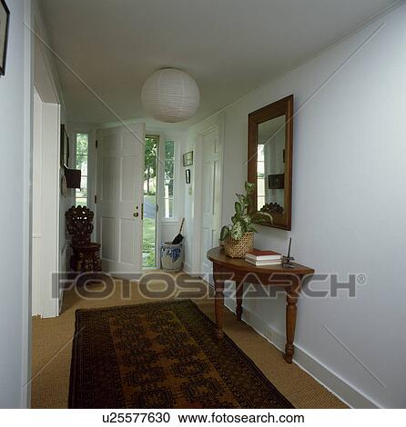 Stock Image - Oriental rug and antique console table in traditional white hall. Fotosearch