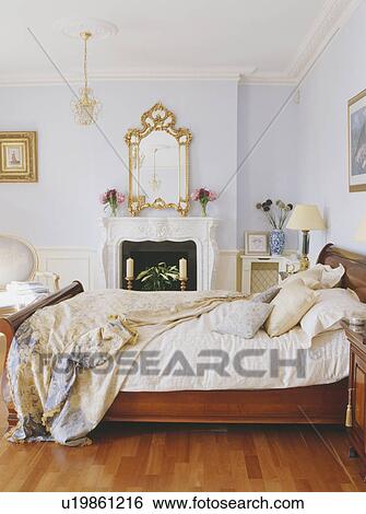 Stock Photograph - Ornate gilt mirror above fireplace in pastel blue bedroo. Fotosearch