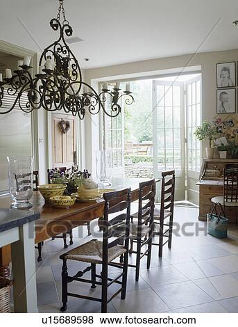 Stock Photo - Ornate metal chandelier above table in dining room with white ceramic floor tiles. Fotosearch