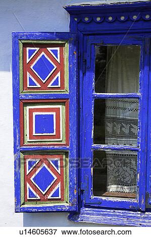 Stock Photo - Painted blue and red traditional pattern on wooden shutter on bright blue Romanian window. Fotosearch