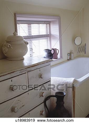 Stock Photo - Painted chest-of-drawers beside bath in small cream cottage bathroom. Fotosearch