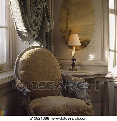 Stock Photo - Painted panel and lighted lamp on console table behind Louis IV style upholstered chair. Fotosearch