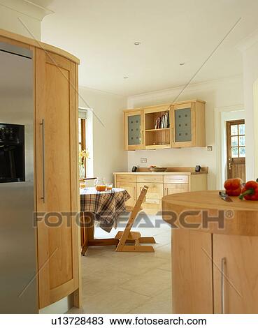 Stock Image - Pale wood fitted units and limestone flooring in modern family kitchen. Fotosearch