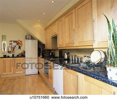 Stock Image - Pale wood fitted units in modern kitchen with white fridge-freezer. Fotosearch