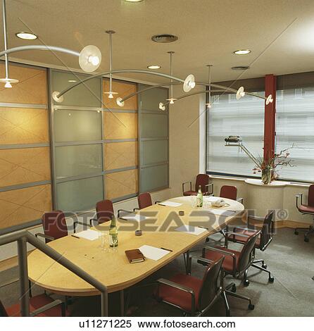 Stock Photography - Pale wood oval table and swivel chairs in meeting room in modern city office. Fotosearch