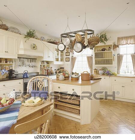 Stock Photo - Pans on rack above island unit with storage baskets on shelves in cream kitchen with parquet flooring. Fotosearch