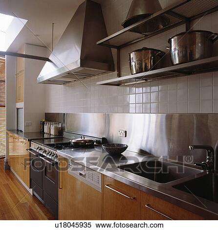Stock Photography - Pans on steel shelves above fitted unit with stainless steel splashback. Fotosearch