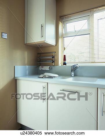 Stock Photography - Pastel blue worktops on white fitted units in modern beige kitchen. Fotosearch