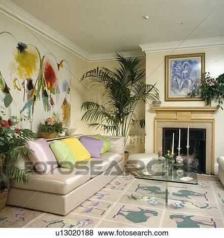 Stock Photo - Pastel cushions on beige silk sofa below large modern painting in living room with pink and green patterned carpet. Fotosearch