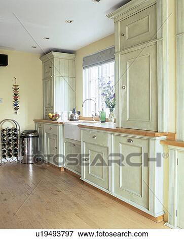 Stock Photo - Pastel green painted wooden cupboards and units in pale yellow kitchen with wooden flooring. Fotosearch