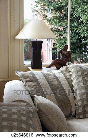 Stock Photograph - Patterned beige cushions on sofa in front of window with white and black lamp on window-sill. Fotosearch