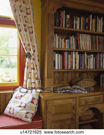 Stock Photography - Patterned curtains on window with matching cushion on window-seat beside fitted bookcase in traditional dining room. Fotosearch