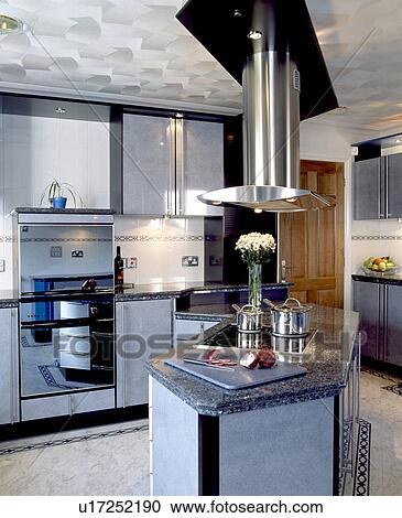 Stock Image - Patterned metallic ceiling in modern kitchen with stainless steel extractor above island unit. Fotosearch